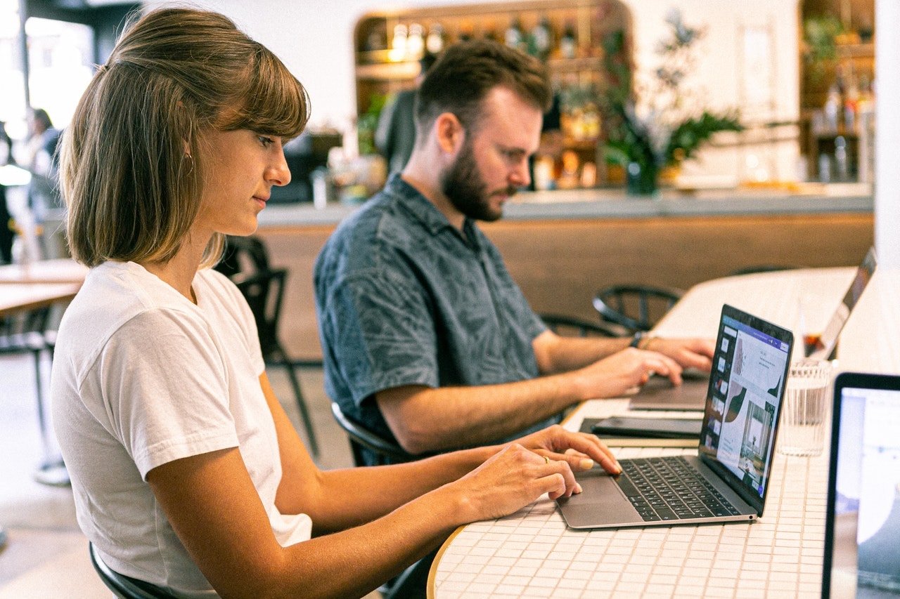 Mujer con blusa color blanca trabajando en computadora junto a  hombre con camisa azul 