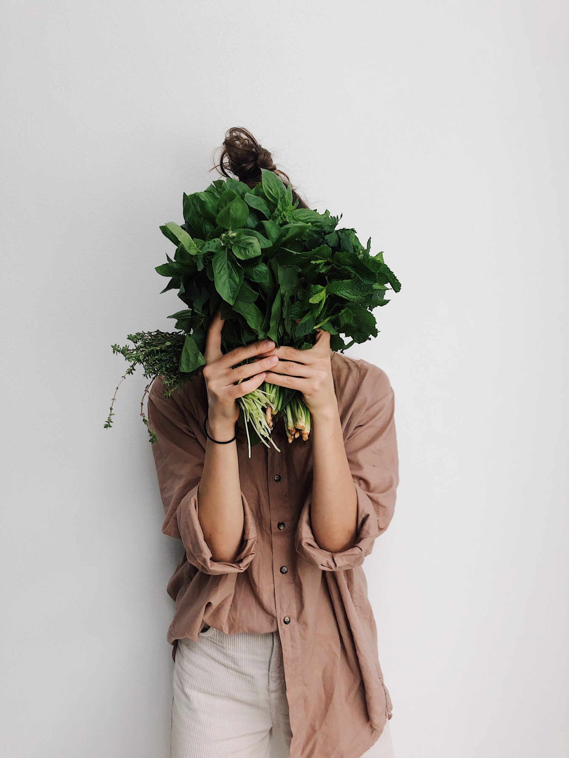 Mujer sosteniendo espinaca cubriéndose la cara: dieta vegana