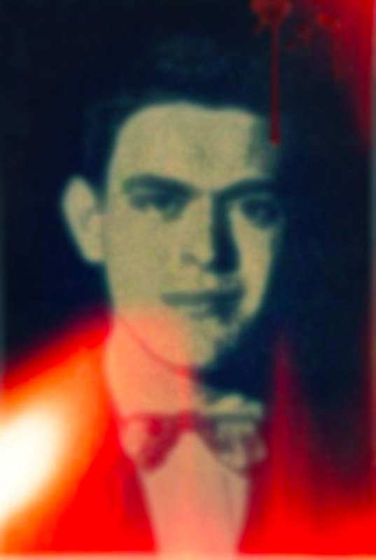 Fotografia antigua de un hombre con traje. En la parte de arriba se nota unas manchas rojas al igual que abajo.