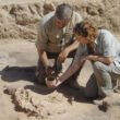 Pareja de mujer y hombre vestidos de color arena, observando una pieza arqueológica