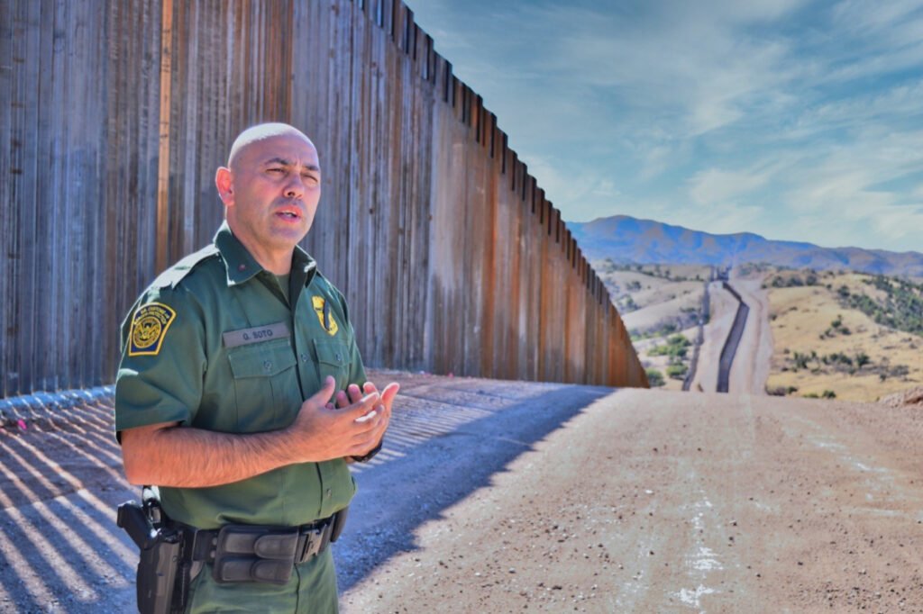 Hombre con uniforme color verde, parado en el muro que separa de Nogales Arizona a Nogales Sonora.