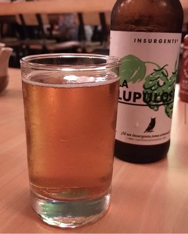 Vaso de cerveza clara, al fondo botella de cerveza con etiqueta blanca con toques color verde
