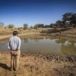 Hombre con camisa color azul y pantalon café claro, observando la sequía de agua en la naturaleza.
