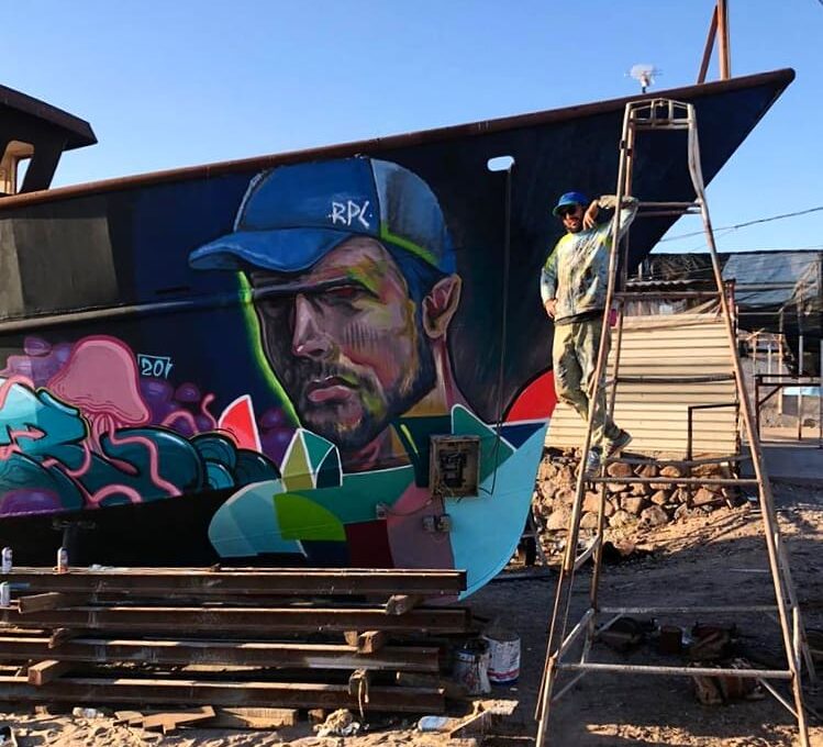 hombre sobre escalera al lado de un mural pintado en un barco varado