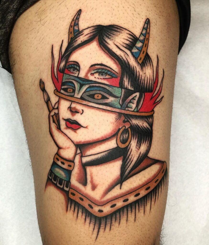 Tatuaje neotradicional de una mujer que tiene partida la cabeza. Tiene cuernos color azul, boca roja, cuatro ojos y aretes dorados.