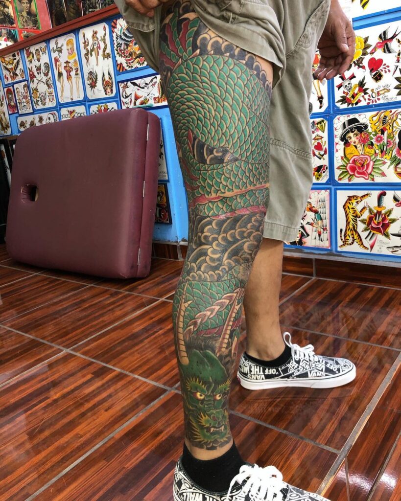 Pierna del lado derecho con tatuaje gigante de un dragón color verde.