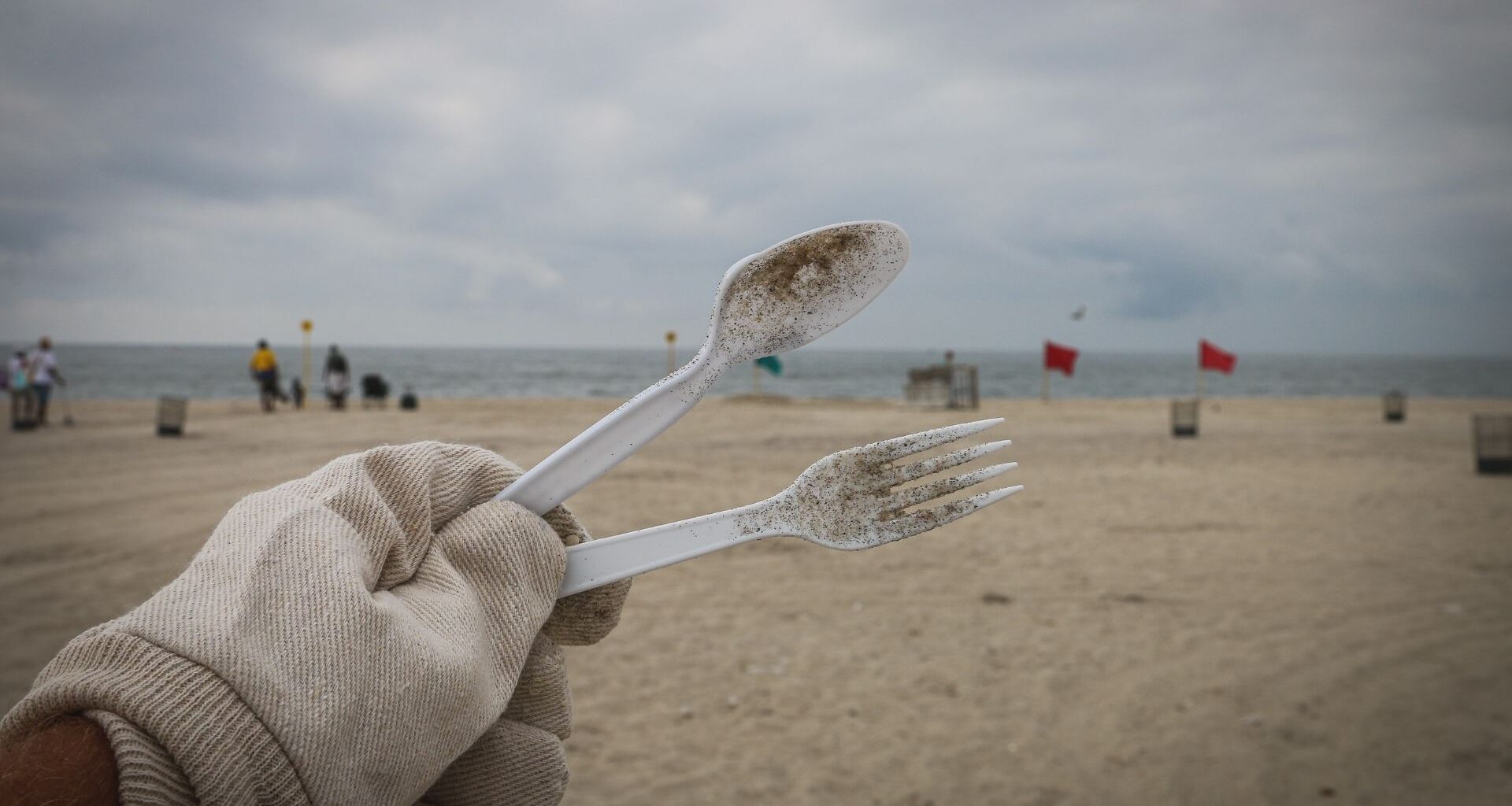 mano sostiene cubiertos de plástico en la playa
