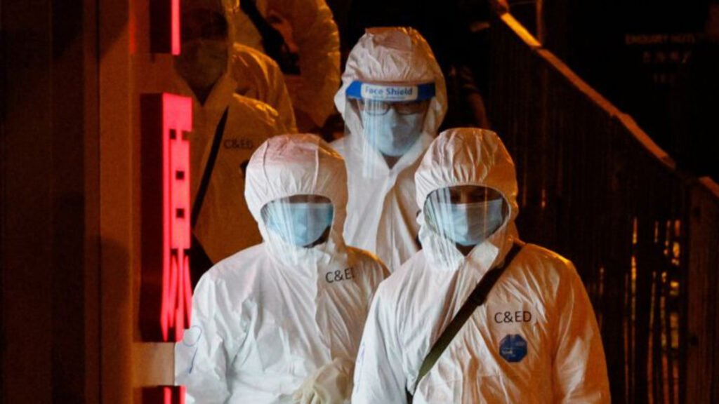 Grupo de tres personas con traje color blanco, careta transparente y cubrebocas color azul. 

En busca del origen del coronavirus.