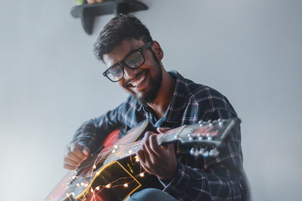 Informe mundial de la felicidad. Hombre con camisa de cuadros color verde oscuro y detalles color blanco. En sus manos tiene una guitarra color rojo con negro.
