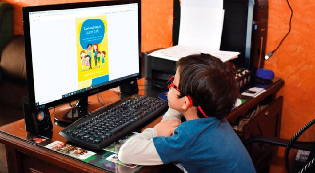 Niño con anteojos color rojo, camisa azul con blanco observando la pantalla de computadora.