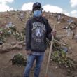 hombre con sudadera que dice Tijuana, gorra y cubrebocas sostiene un palo en medio del cementerio