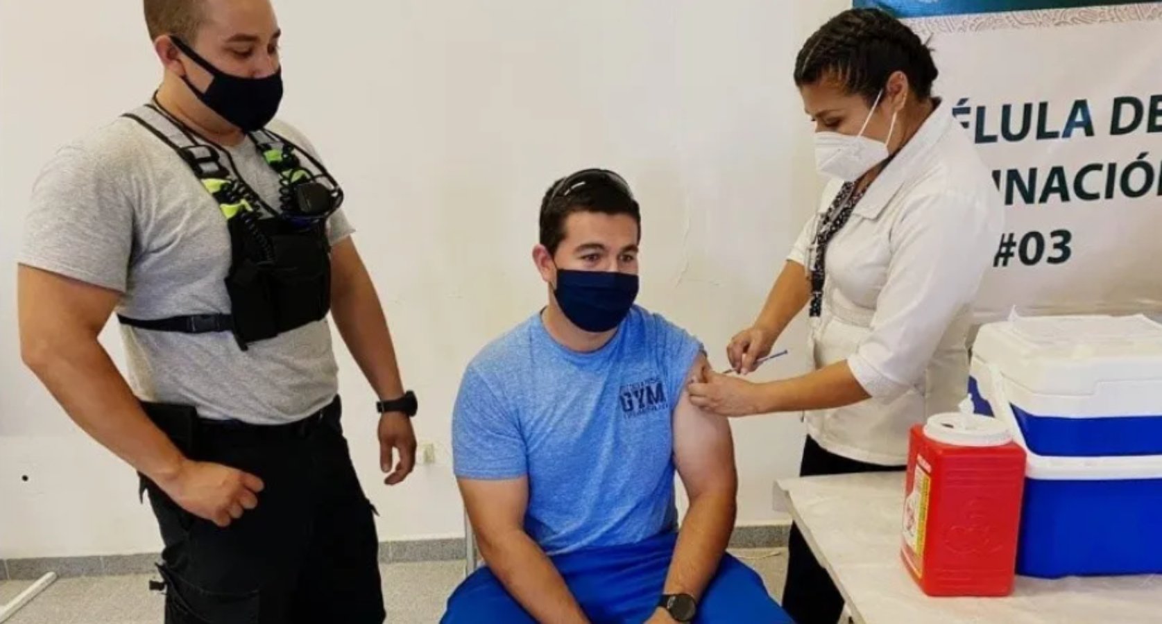 Vacunación de Bomberos; hombre vestido de azul con cubrebocas es vacunado en el brazo izquierdo por mujer vestida de blanco