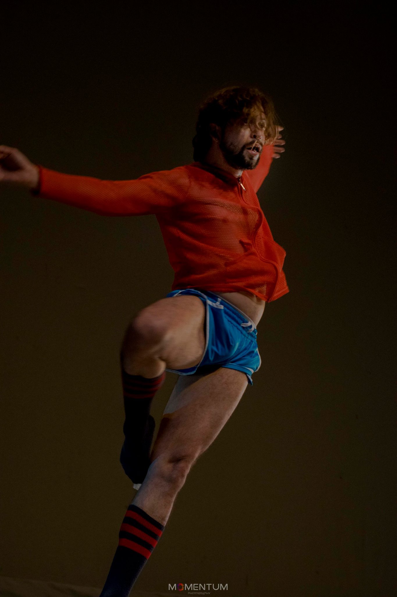 hombre baila con shorts azules y camiseta naranja, alza los brazos