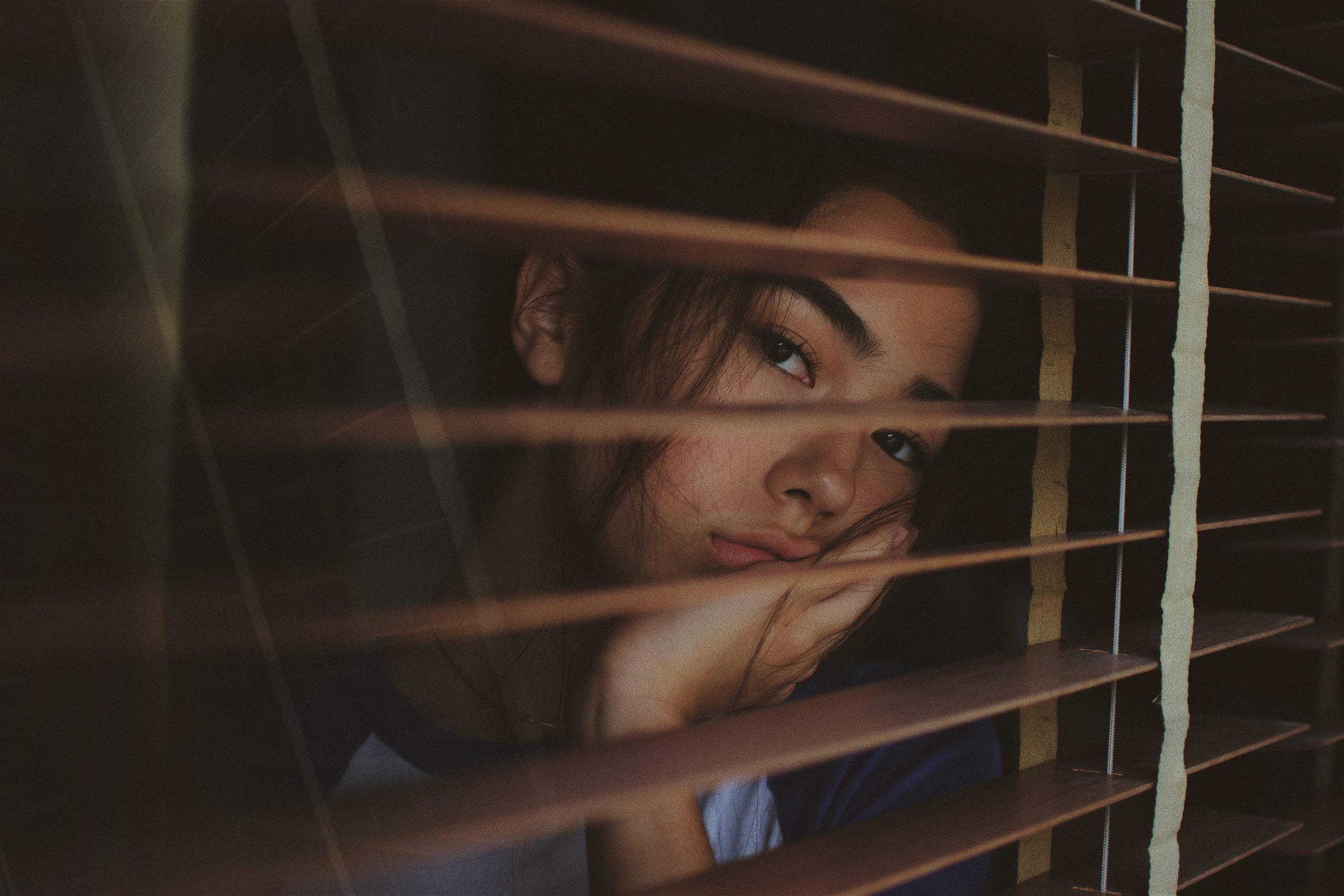Mujer joven con mirada triste mirando por una ventana. 