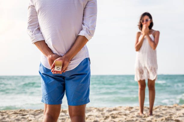 Propuesta de matrimonio a la orilla de la playa. Novio le da anillo de compromiso a novia en un destino turistico