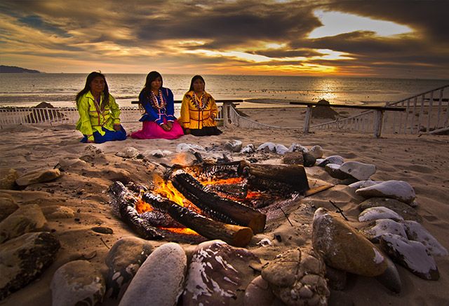 Mujeres seris sentadas en la playa frente a una fogata al atardecer