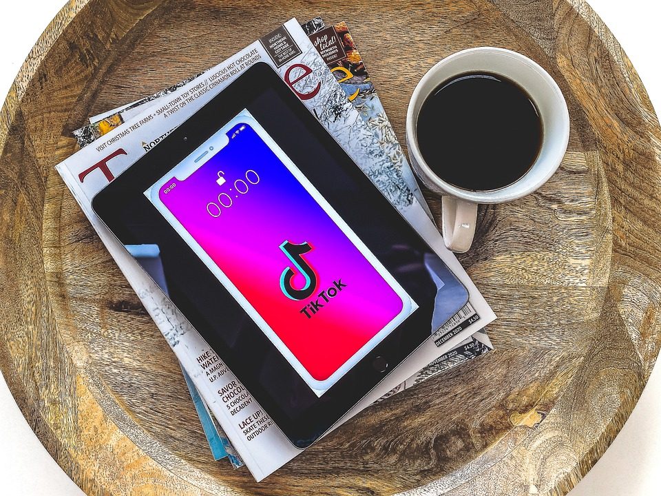 Celular smartphone con la aplicacion de TikTok arriba de una mesa con revistas y una taza de cafe