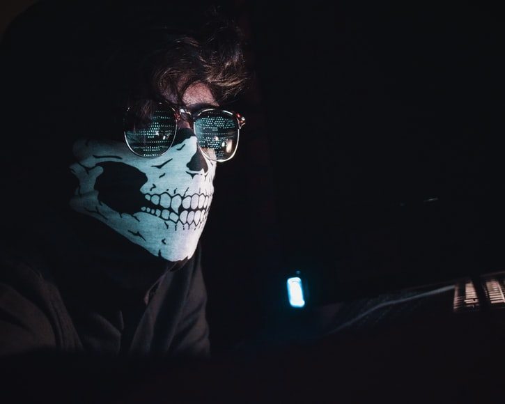 Hacker con lentes oscuros y tapabocas hackenado en una computadora 