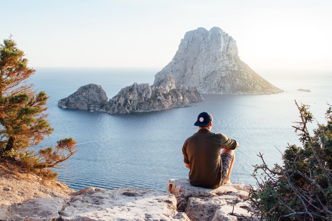 Una persona sentada, se ve su espalda y que porta una gorra azul. De fondo se ve el mar y una isla rocosa. destinos turísticos del noroeste