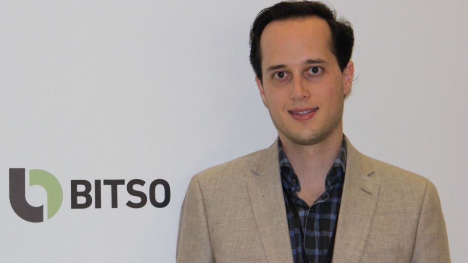 It's Daniel Vogel, a young man in the foreground. In the background we can see the logo of his company: Bitso.
Daniel wears a plaid shirt and a cream-colored jacket.
