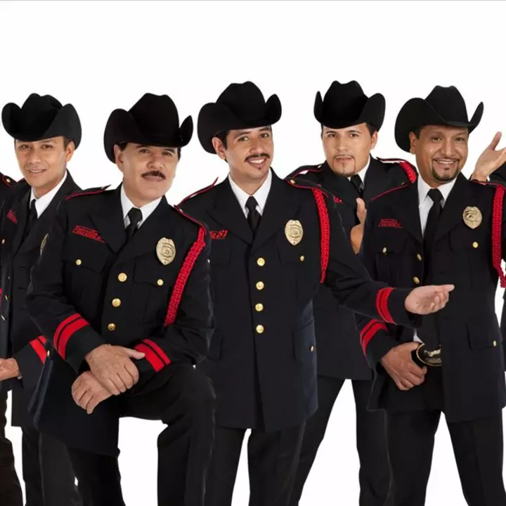 Se muestran cinco hombres que conforman una banda. Todos con ropa y sombrero negro.