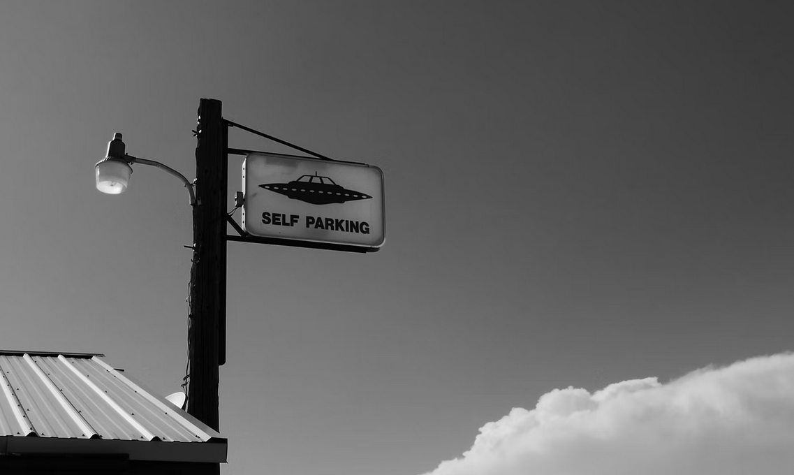 Imagen a blanco y negro. Un poste con un letrero con imagen de OVNI