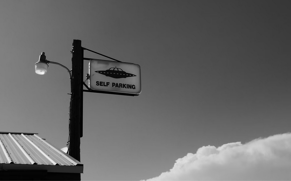 Imagen a blanco y negro. Un poste con un letrero con imagen de OVNI