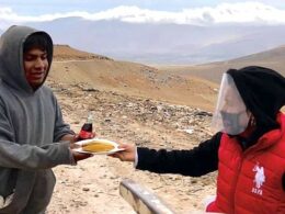 Una persona con careta de protección por covid-19 entrega comida a un hombre con capucha gris.