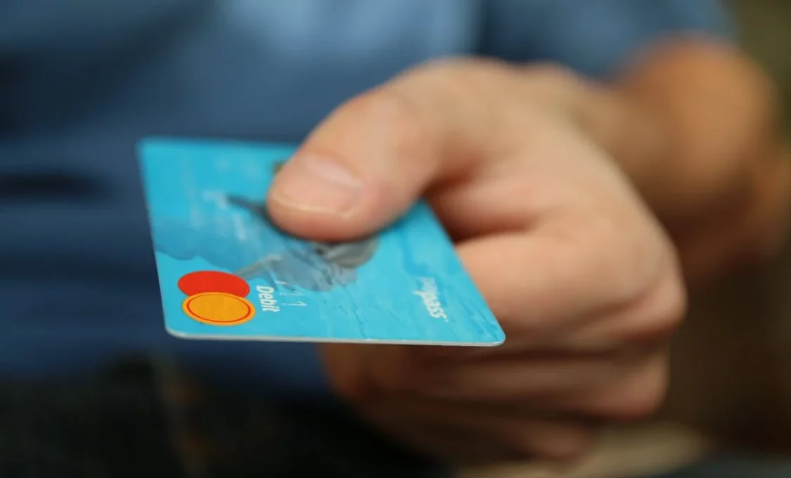 Una persona extiende una tarjeta bancaria azul.