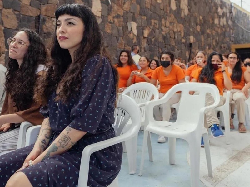 Mon Laferte atenta en el Cereso de Ciudad Obregón, Sonora. Hay una pared de piedra de fondo y mujeres con camisetas naranjas.