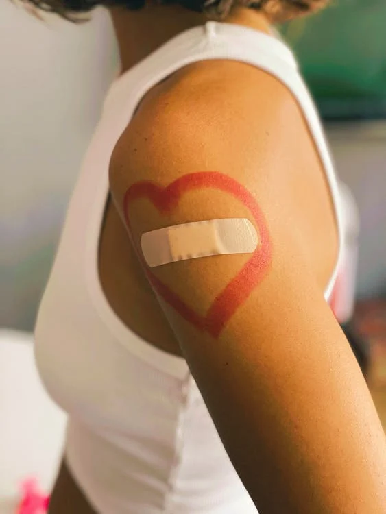 El brazo de una mujer que acaba de vacunarse. Hay una curita rodeada por un corazón rojo. Vacuna covid altera ciclos menstruales. 