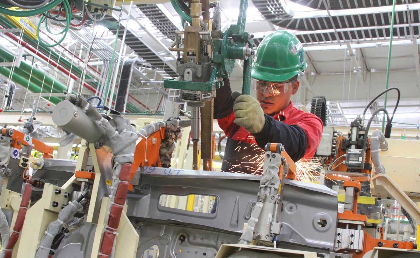 Un hombre trabaja en una maquinaria industrial. Porta casco verde.