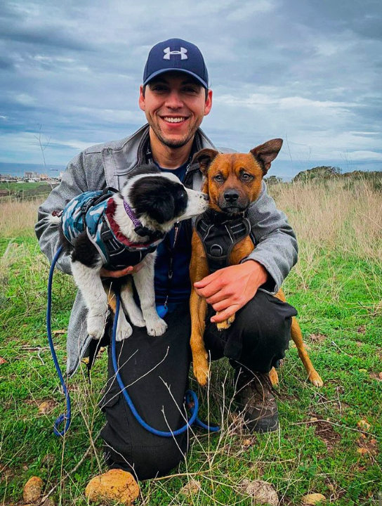 Pedro Silva con dos perros en sus brazos. Están en un área despejada y natural.