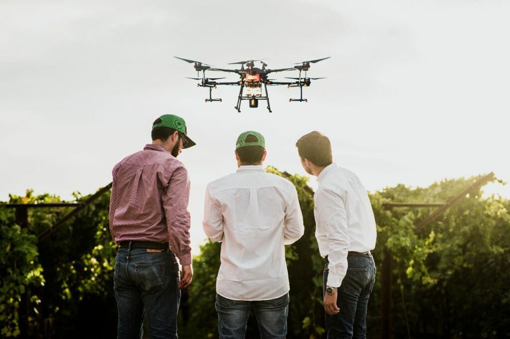 tres hombres de espaldas en campo agrícola manejan dron