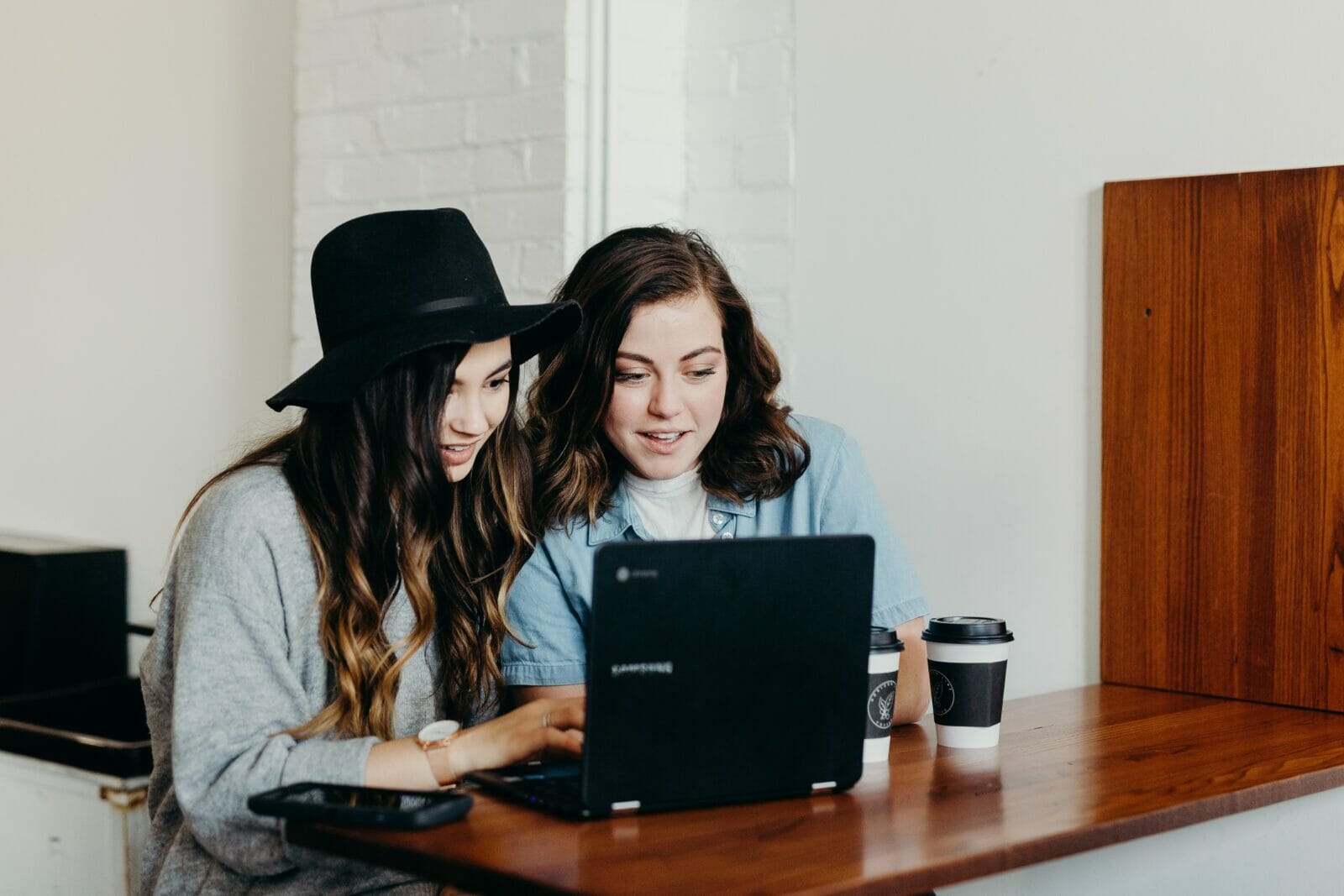 dos mujeres jóvenes ven algo en una computadora personal beben café