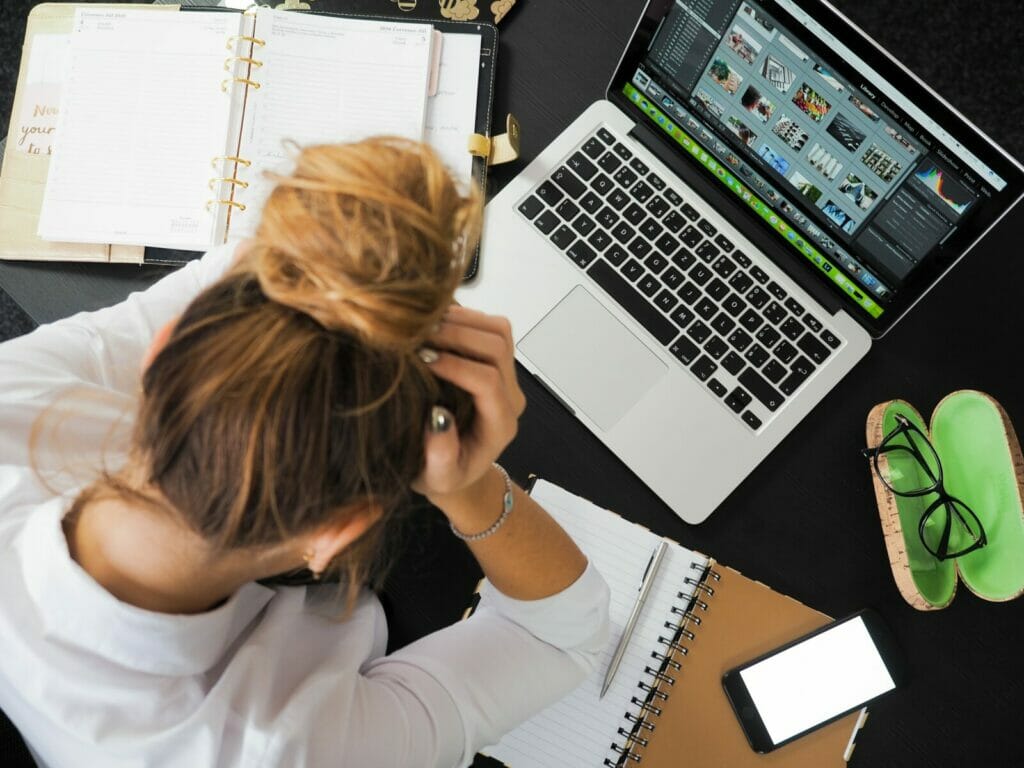 Tired woman sitting in front of a desktop computer with a notebook beside her. 