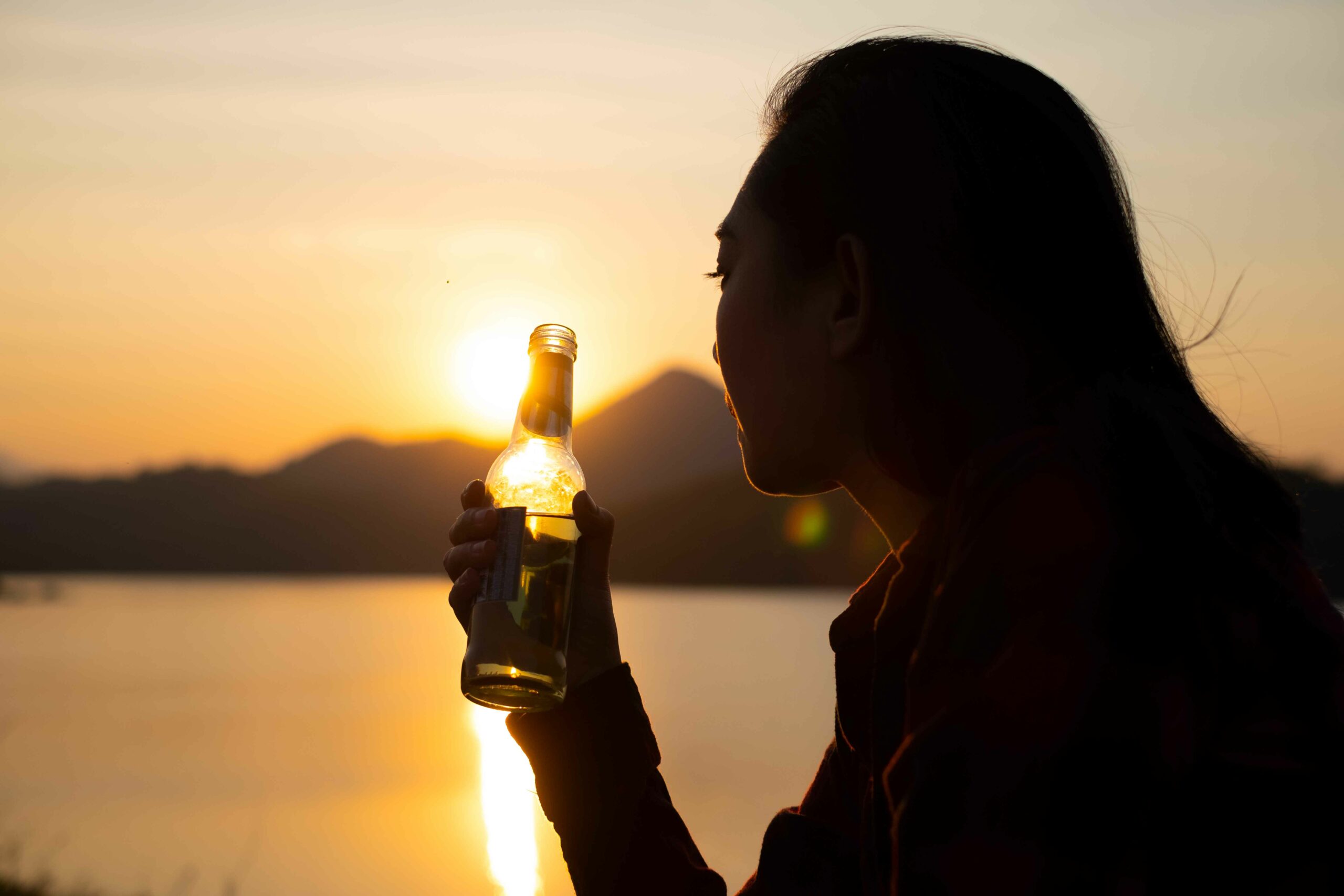 Mujer tomando una botella de cerveza frente al mar.