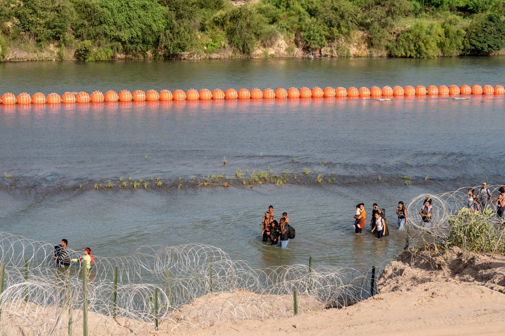 Migrantes caminan por el Río Bravo a unos metros de las boyas que colocó el gobierno de Texas.